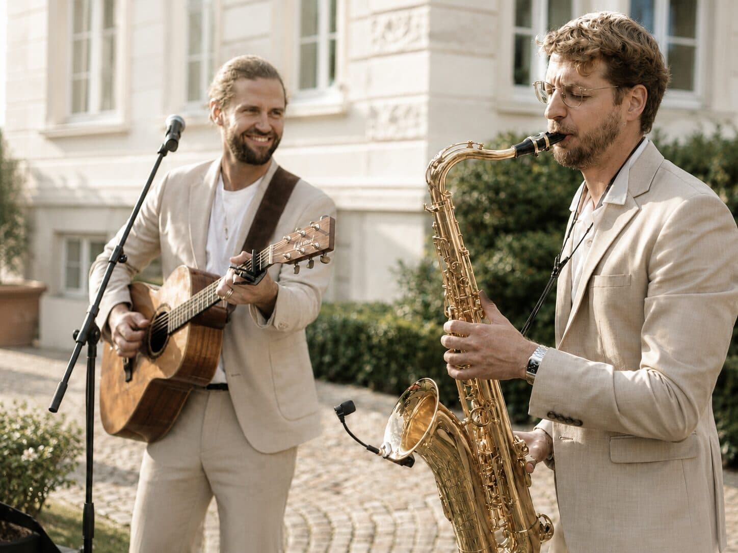 A guitarist and saxophonist performing together outdoors.